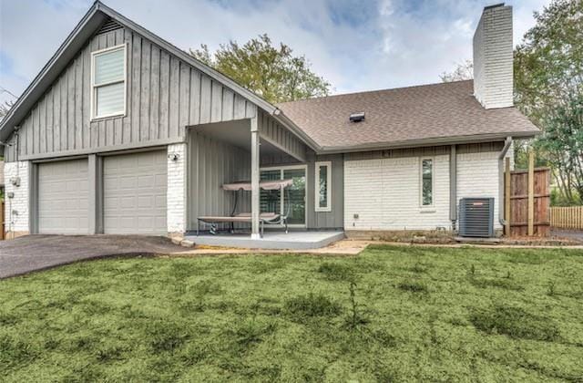 rear view of property featuring a garage, central AC unit, and a yard