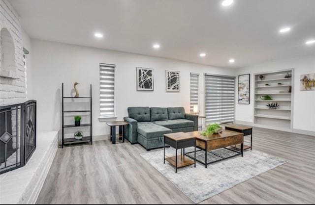 living room featuring built in shelves, a healthy amount of sunlight, light hardwood / wood-style floors, and a fireplace