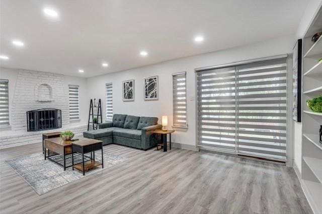 living room featuring a brick fireplace, light wood-type flooring, and plenty of natural light