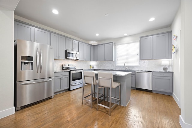 kitchen featuring a kitchen bar, appliances with stainless steel finishes, decorative backsplash, a kitchen island, and light stone counters