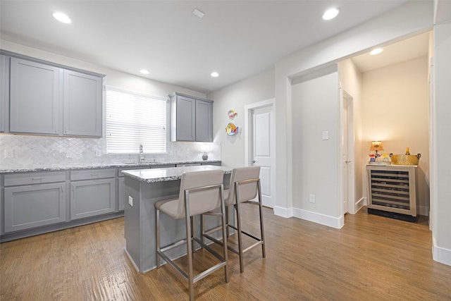 kitchen with gray cabinetry, a kitchen island, light stone countertops, and beverage cooler