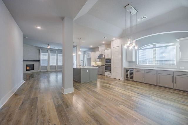 kitchen featuring a wealth of natural light, decorative light fixtures, white cabinetry, stainless steel oven, and a center island with sink