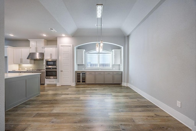 kitchen featuring beverage cooler, white cabinetry, stainless steel appliances, decorative backsplash, and vaulted ceiling