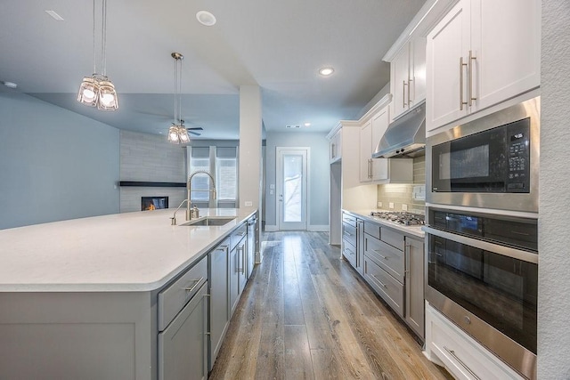 kitchen featuring white cabinetry, pendant lighting, backsplash, stainless steel appliances, and a center island with sink