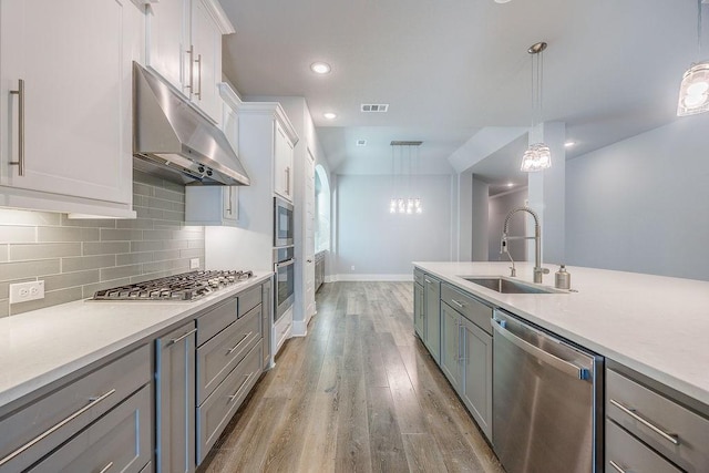 kitchen featuring white cabinetry, sink, light wood-type flooring, pendant lighting, and stainless steel appliances