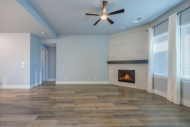 unfurnished living room featuring a tile fireplace, dark hardwood / wood-style floors, and ceiling fan