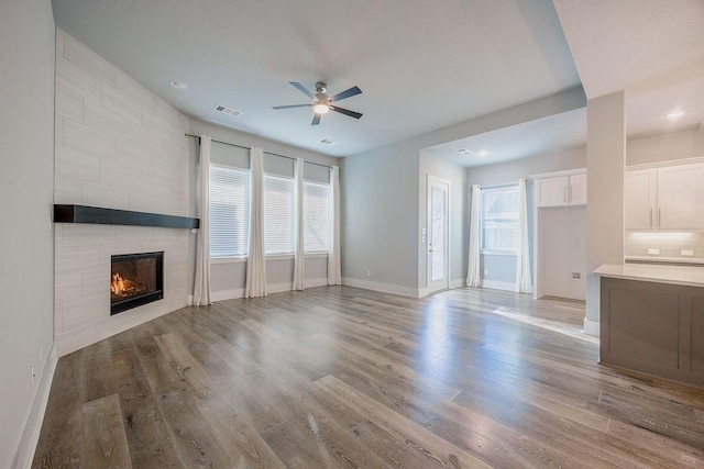 unfurnished living room featuring light wood-type flooring, ceiling fan, and a tiled fireplace