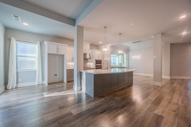 kitchen with built in microwave, hanging light fixtures, a large island, hardwood / wood-style flooring, and white cabinetry