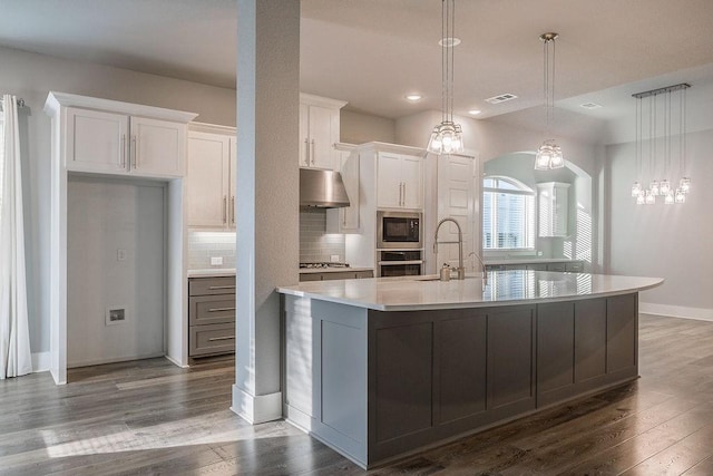 kitchen with a large island with sink, white cabinetry, stainless steel appliances, tasteful backsplash, and hanging light fixtures