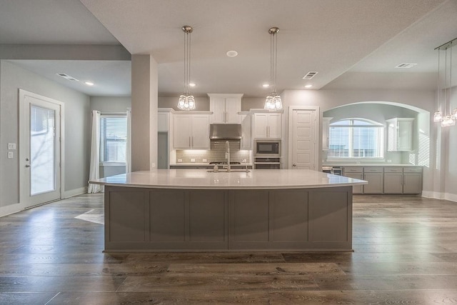 kitchen featuring a large island with sink, dark wood-type flooring, white cabinetry, black microwave, and decorative backsplash