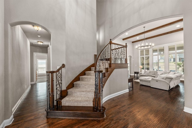 stairway with a high ceiling, wood-type flooring, beamed ceiling, and an inviting chandelier