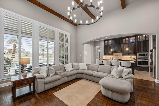 living room with a towering ceiling, dark wood-type flooring, a chandelier, and beamed ceiling