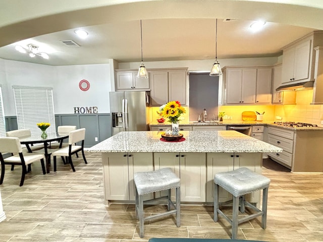 kitchen with sink, hanging light fixtures, a center island, light stone counters, and stainless steel appliances