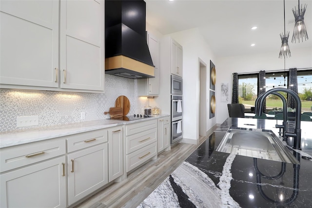 kitchen featuring light stone countertops, premium range hood, white cabinetry, backsplash, and stainless steel appliances