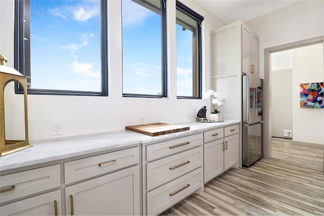 kitchen with light stone counters, white cabinets, stainless steel fridge, and light hardwood / wood-style flooring