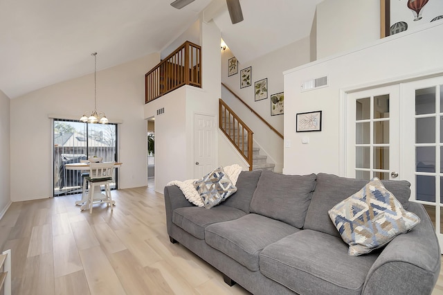 living room featuring light wood-type flooring, french doors, ceiling fan with notable chandelier, and high vaulted ceiling