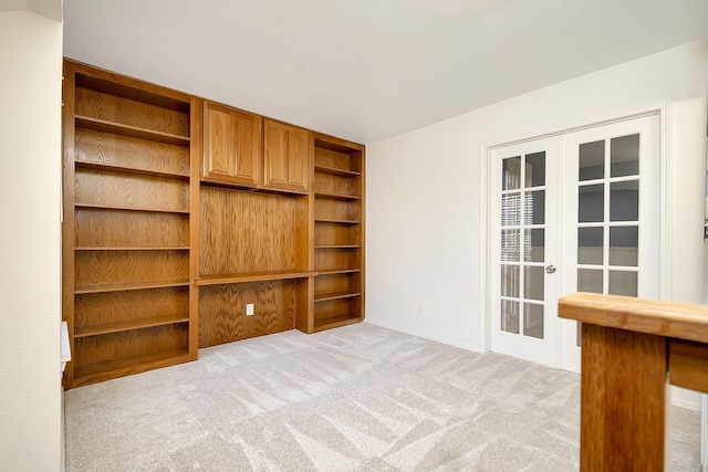 unfurnished living room with light carpet, built in shelves, and french doors