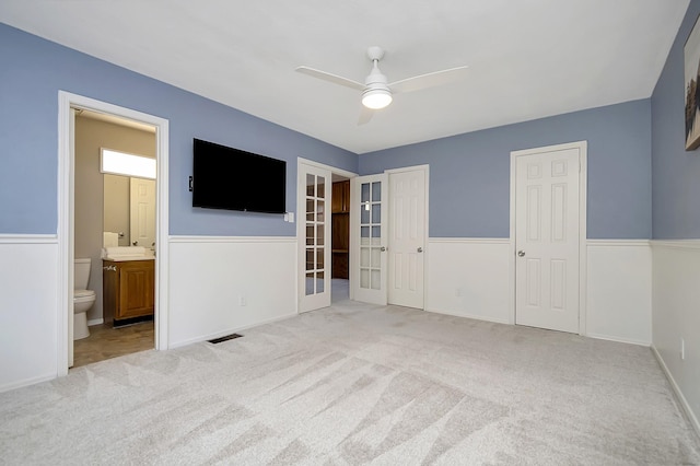 interior space with ceiling fan, french doors, light carpet, and ensuite bath