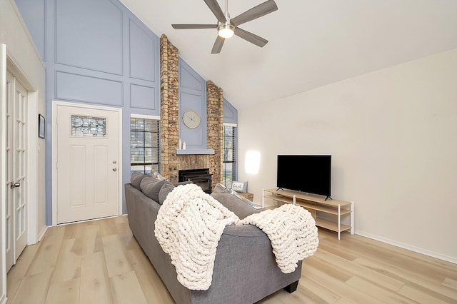 living room with light hardwood / wood-style floors, high vaulted ceiling, a brick fireplace, and ceiling fan