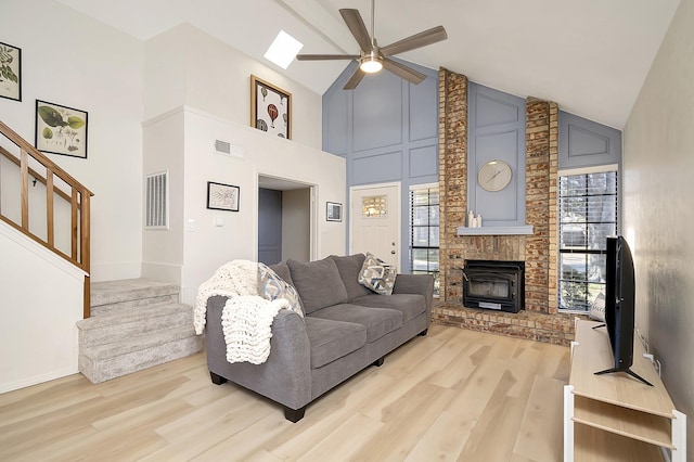 living room with light wood-type flooring, ceiling fan, high vaulted ceiling, and a brick fireplace