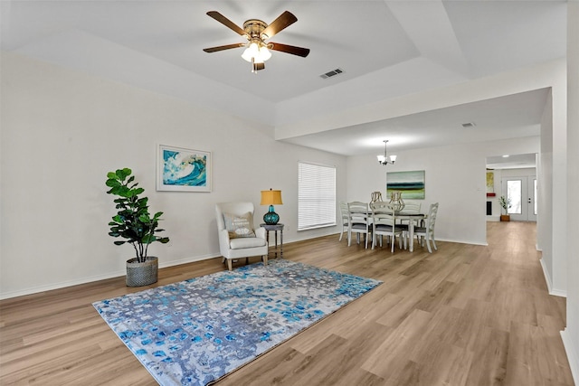 sitting room featuring ceiling fan with notable chandelier, light hardwood / wood-style floors, and a tray ceiling