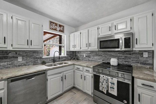 kitchen featuring appliances with stainless steel finishes, sink, white cabinetry, light tile patterned floors, and a textured ceiling