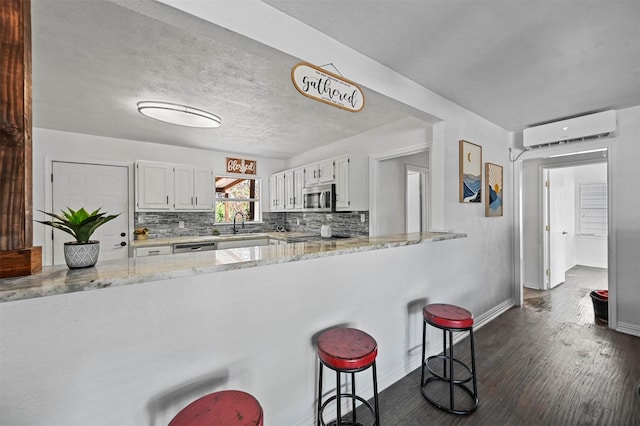 kitchen with a wall mounted air conditioner, light stone countertops, white cabinetry, and appliances with stainless steel finishes