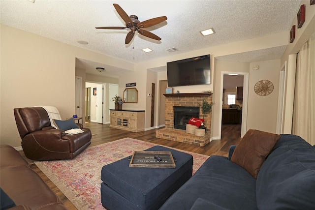 living room with ceiling fan, a fireplace, dark hardwood / wood-style floors, and a textured ceiling