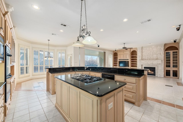 kitchen with a center island, decorative light fixtures, a stone fireplace, light tile patterned flooring, and stainless steel gas stovetop