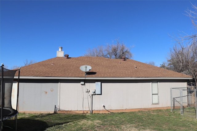 rear view of property featuring a trampoline and a lawn