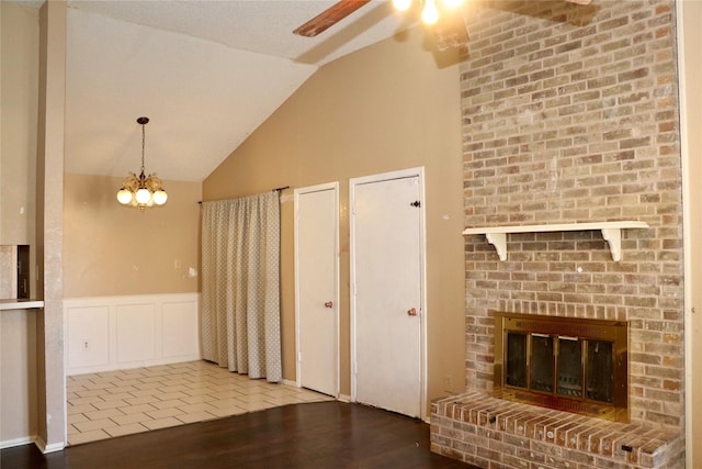 unfurnished living room featuring hardwood / wood-style flooring, a fireplace, ceiling fan with notable chandelier, and vaulted ceiling