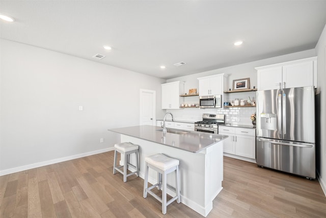 kitchen featuring a kitchen island with sink, sink, white cabinets, backsplash, and stainless steel appliances