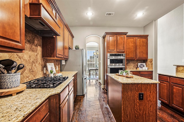 kitchen with light stone countertops, appliances with stainless steel finishes, custom exhaust hood, a kitchen island, and dark wood-type flooring