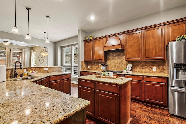 kitchen with stainless steel refrigerator with ice dispenser, hanging light fixtures, custom range hood, sink, and a center island