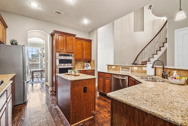 kitchen featuring appliances with stainless steel finishes, hanging light fixtures, sink, a kitchen island, and dark hardwood / wood-style flooring