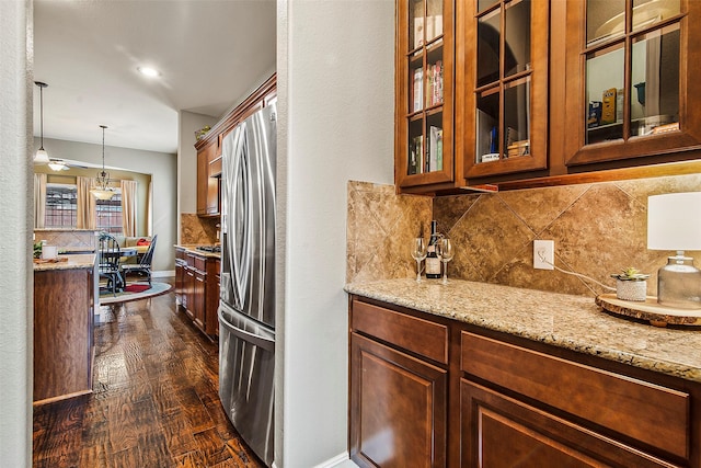 kitchen with dark wood-type flooring, light stone countertops, stainless steel fridge, and hanging light fixtures