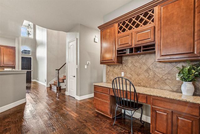 kitchen with backsplash, dark hardwood / wood-style floors, light stone countertops, and built in desk