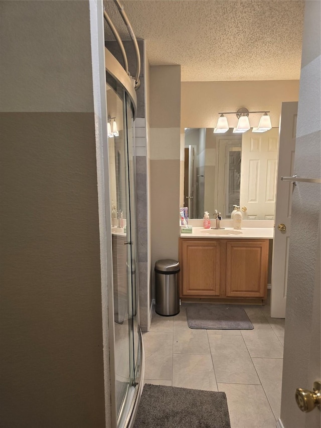 bathroom with a textured ceiling, tile patterned flooring, a shower with shower door, and vanity