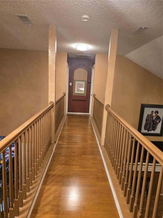 corridor featuring wood-type flooring, a textured ceiling, and lofted ceiling