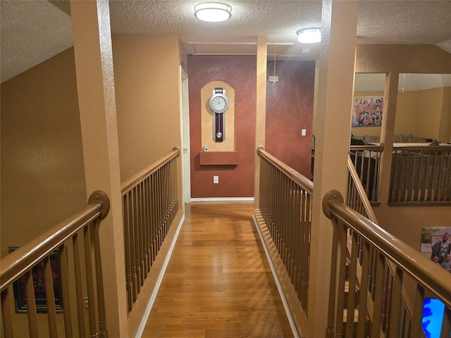 corridor with light hardwood / wood-style flooring, a textured ceiling, and lofted ceiling