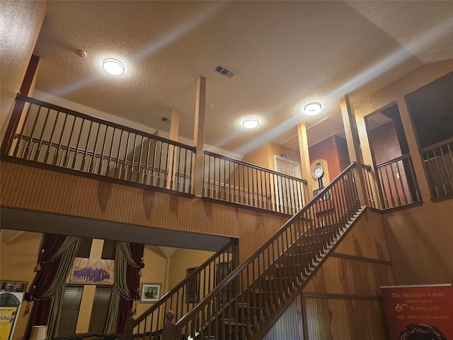 staircase featuring high vaulted ceiling, a textured ceiling, and wood walls