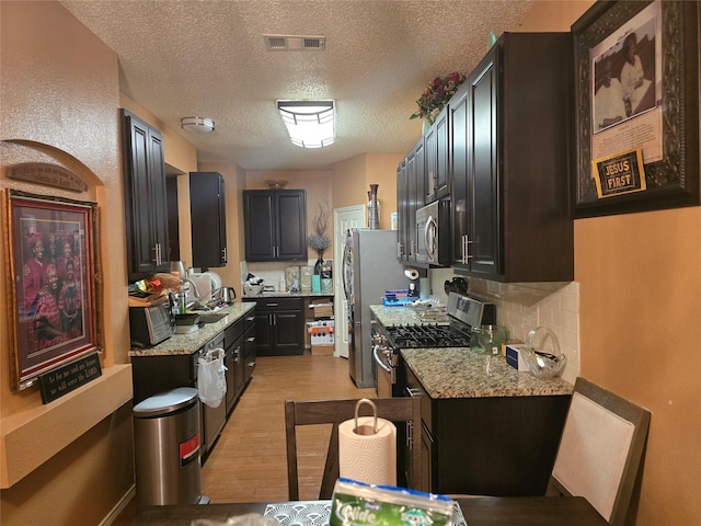 kitchen with light hardwood / wood-style floors, decorative backsplash, light stone countertops, and stainless steel appliances