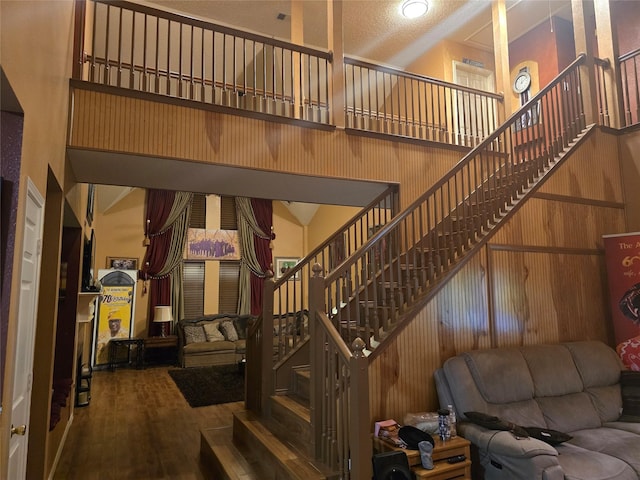 interior space featuring a textured ceiling, hardwood / wood-style floors, a towering ceiling, and wooden walls