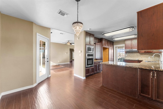 kitchen with appliances with stainless steel finishes, decorative light fixtures, sink, decorative backsplash, and dark stone counters