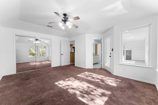 unfurnished bedroom featuring dark carpet, ceiling fan, a raised ceiling, ensuite bath, and a closet