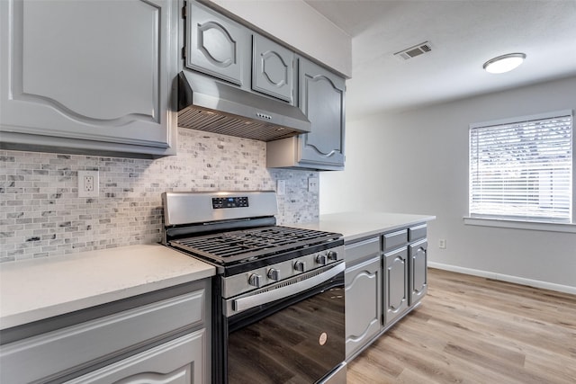 kitchen with exhaust hood, light hardwood / wood-style floors, gray cabinetry, gas stove, and backsplash