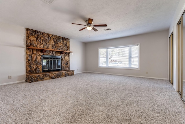 unfurnished living room with ceiling fan, carpet, a textured ceiling, and a stone fireplace