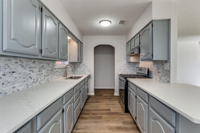 kitchen featuring light hardwood / wood-style flooring, sink, gray cabinets, stainless steel gas range, and decorative backsplash