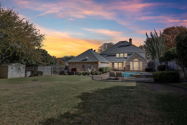 back house at dusk with a storage unit, a fenced in pool, a patio, and a yard