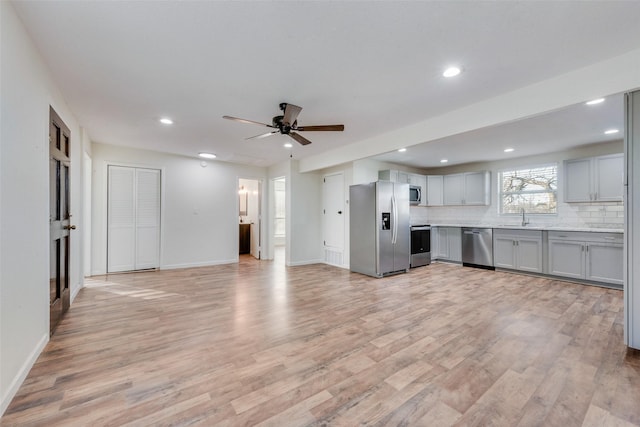 kitchen featuring ceiling fan, light hardwood / wood-style floors, appliances with stainless steel finishes, sink, and backsplash